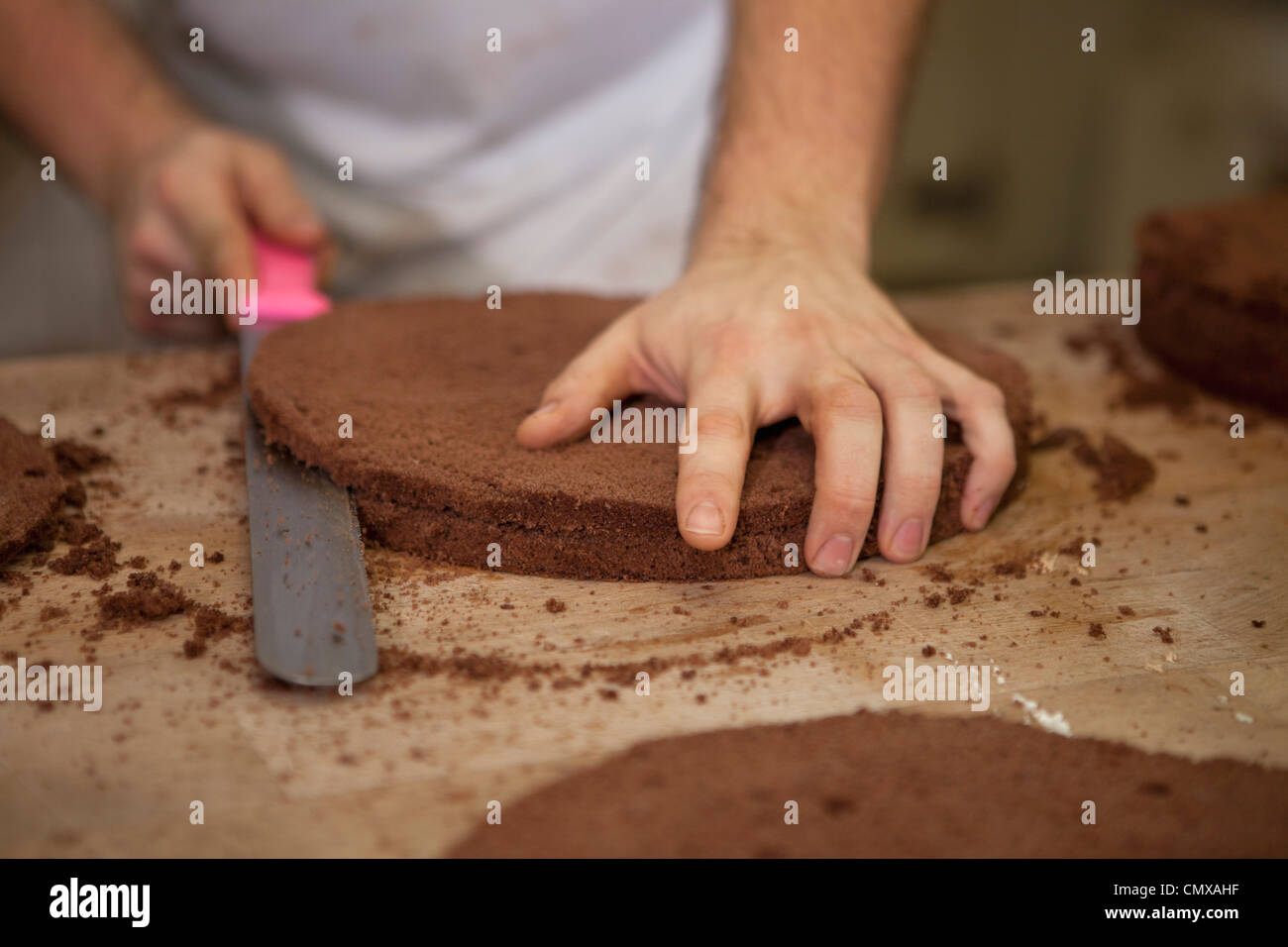 Germany, Bavaria, Munich, Baker cutting cake layers Stock Photo