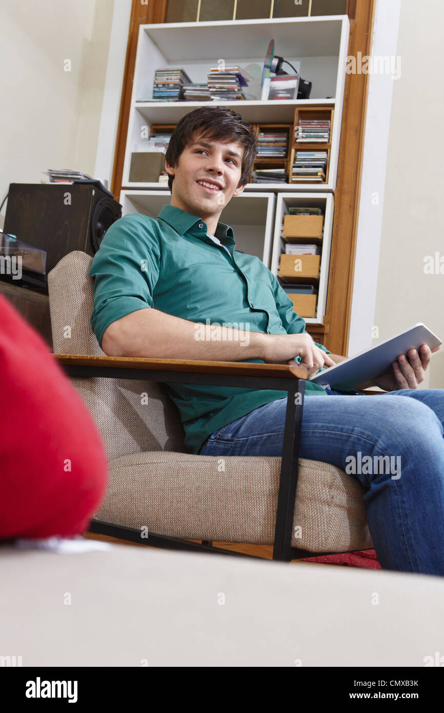 Germany, Cologne, Young man with digital tablet on chair, smiling Stock Photo