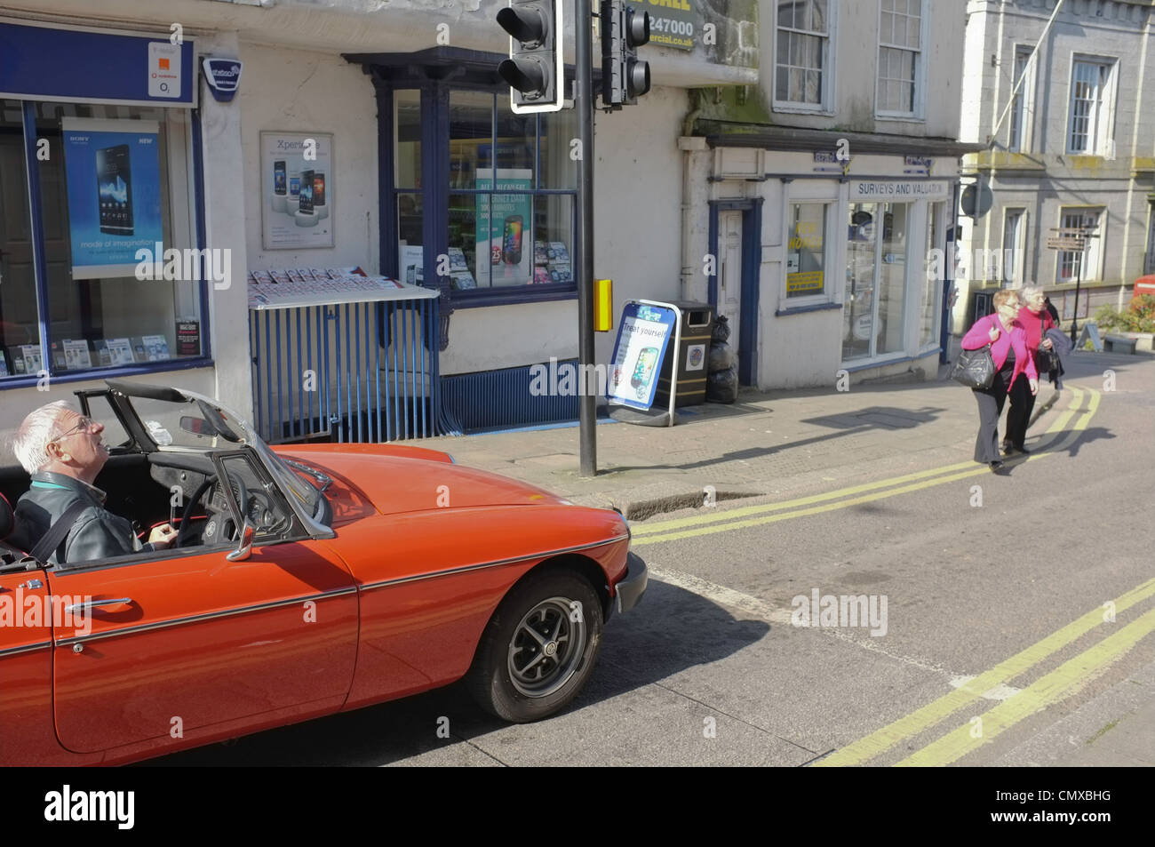 A grey haired man in his late sixties waits at traffic lights in an open-topped sports car in Cornwall, UK Stock Photo