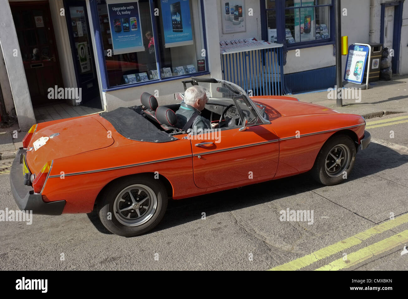A grey haired man in his late sixties waits at traffic lights in an open-topped sports car Stock Photo
