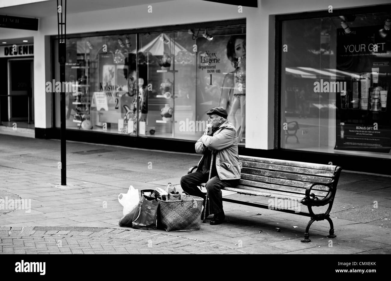 Old man sat alone on a town centre bench with shopping Stock Photo