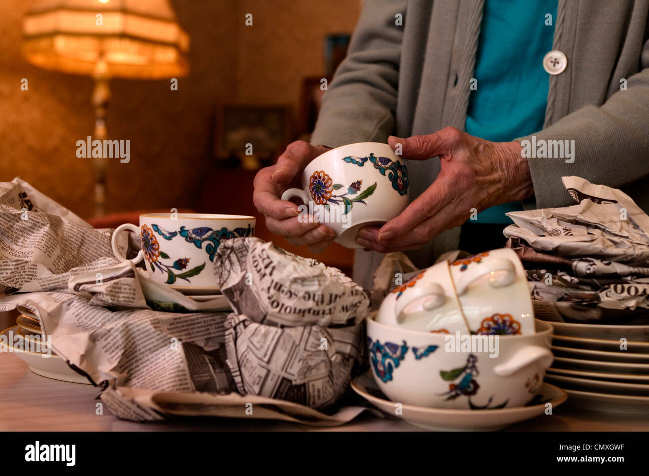 Elderly lady wrapping up cups and saucers from a set of china, in newspaper, ready for storage or moving Stock Photo