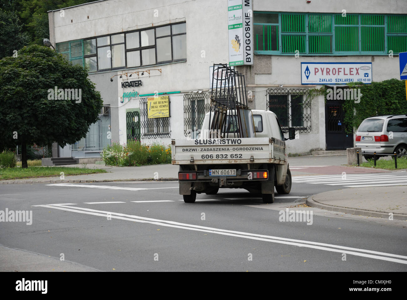 Small, light commercial vehicle turning right on crossroads. Truck carries frame with windows. Stock Photo