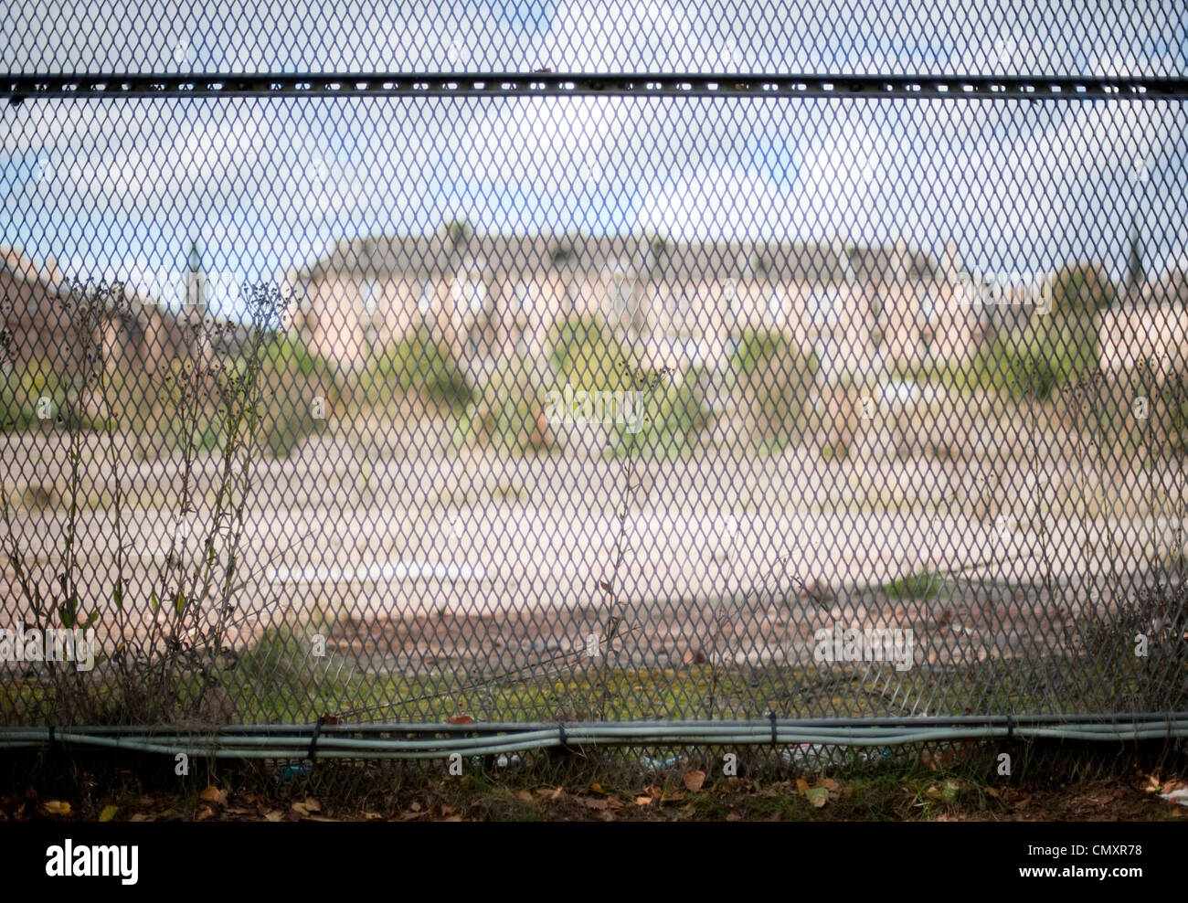 A derelict waste ground and buildings are out of focus behind a wire fence in Glasgow Stock Photo
