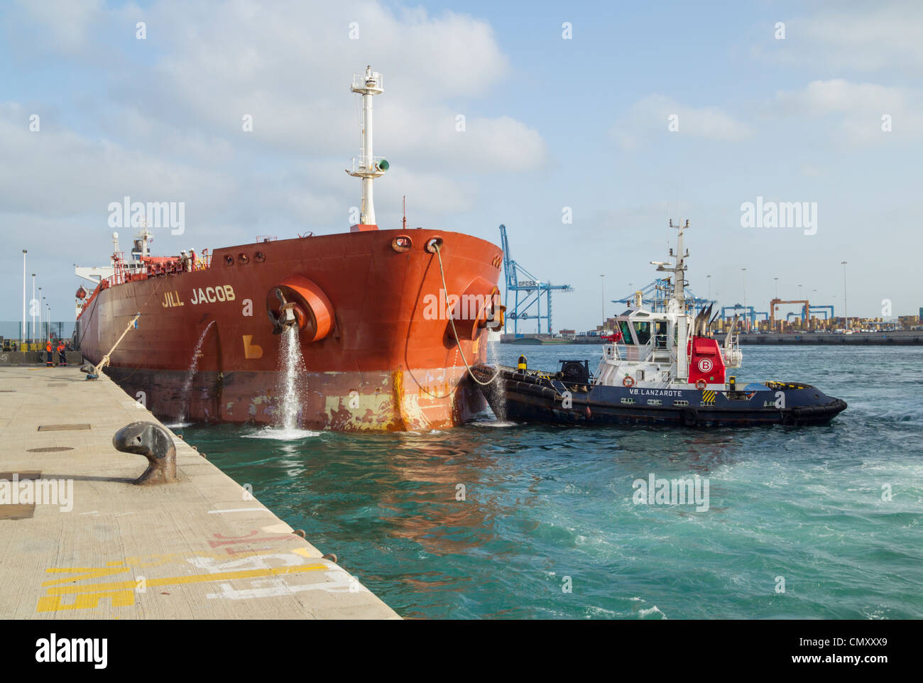 Oil tanker pumping ballast water as tug boat guides ship onto berth