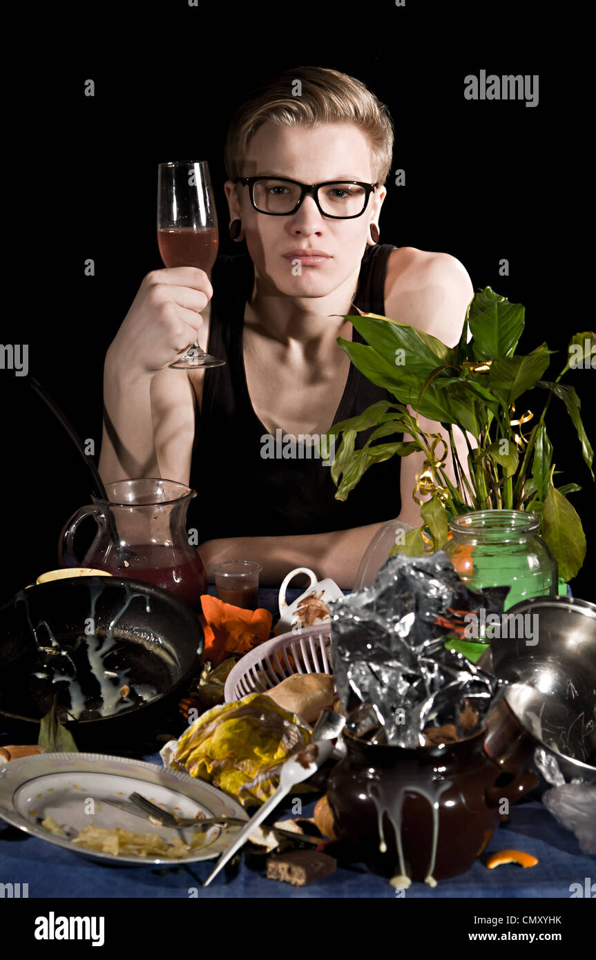 A young man with a glass sits behind dirty table Stock Photo