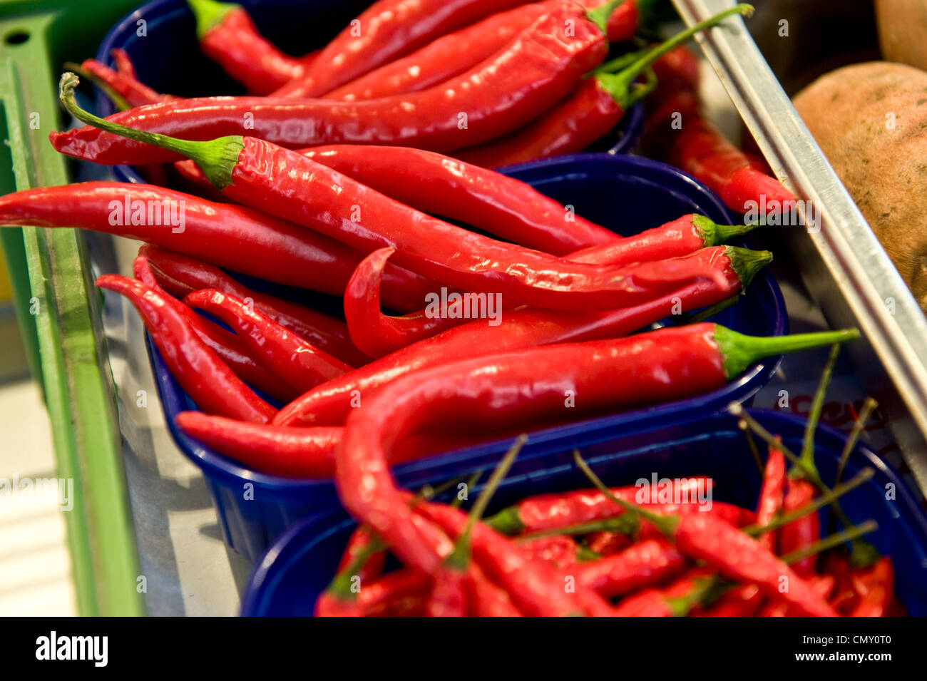 A closeup shot of glazed, shiny cayenne peppers grouped in mini blue baskets on a green tray in a food market. Stock Photo