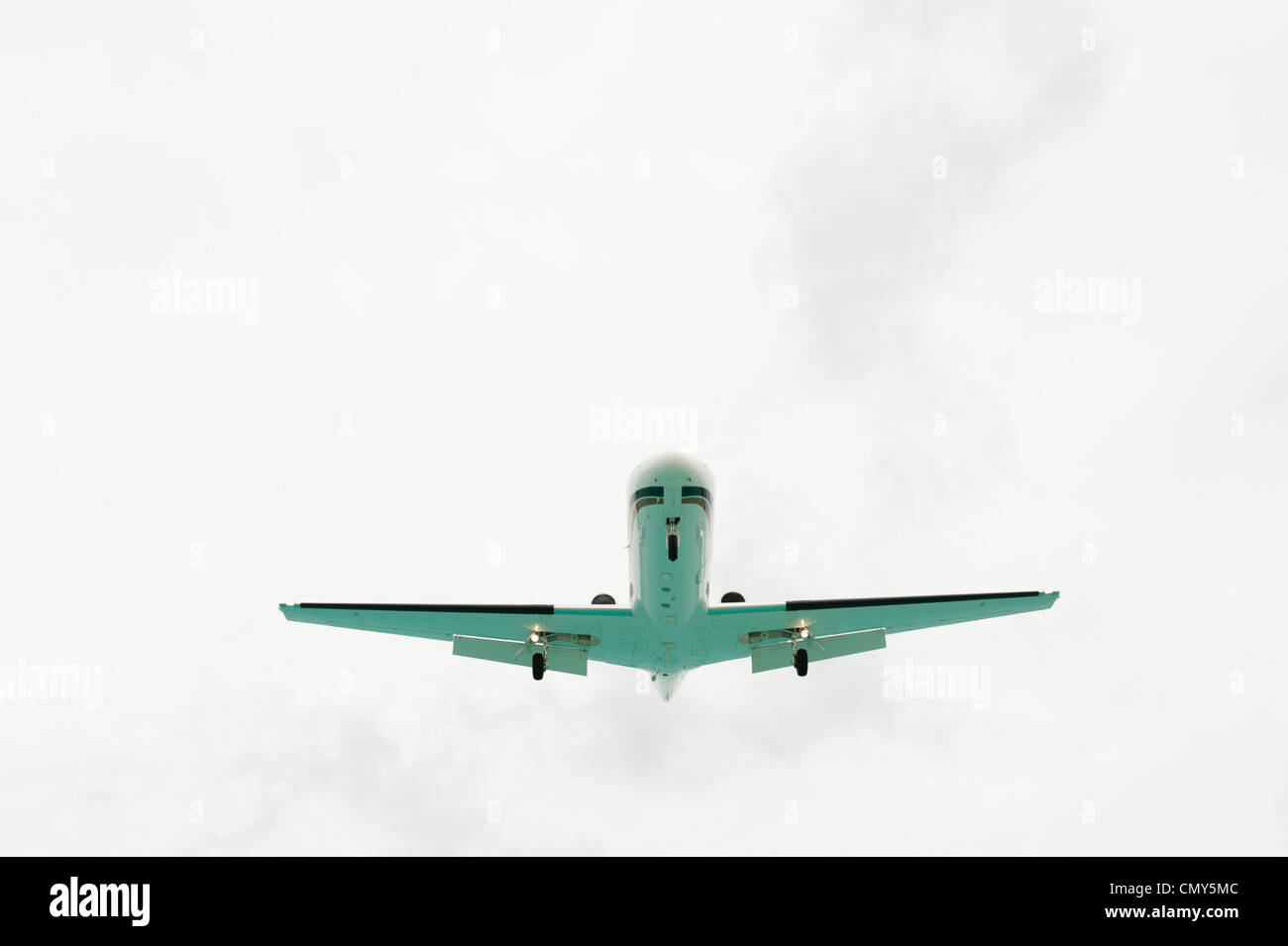 A shot taken on the ground of the bottom of an airplane flying in a cloudy sky. Stock Photo