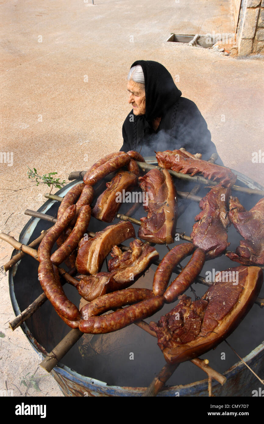 An old Maniat lady from Dryalos village, is preparing 'syglino' (also known as 'pasto'=smoked pork) and sausages. Mani, Greece. Stock Photo