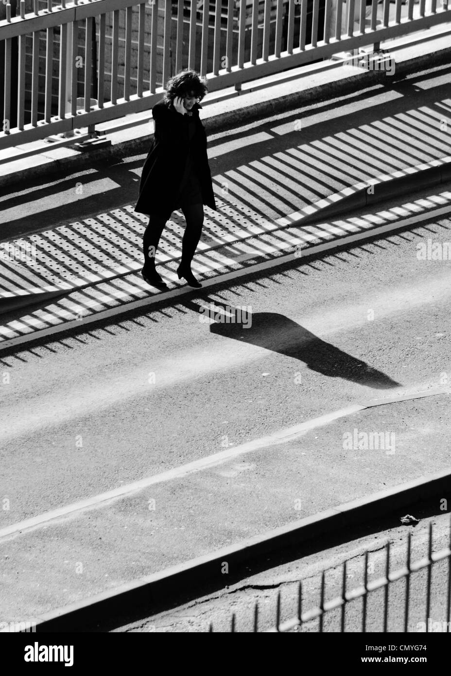 Woman crossing a street on the phone, strong shadow Stock Photo