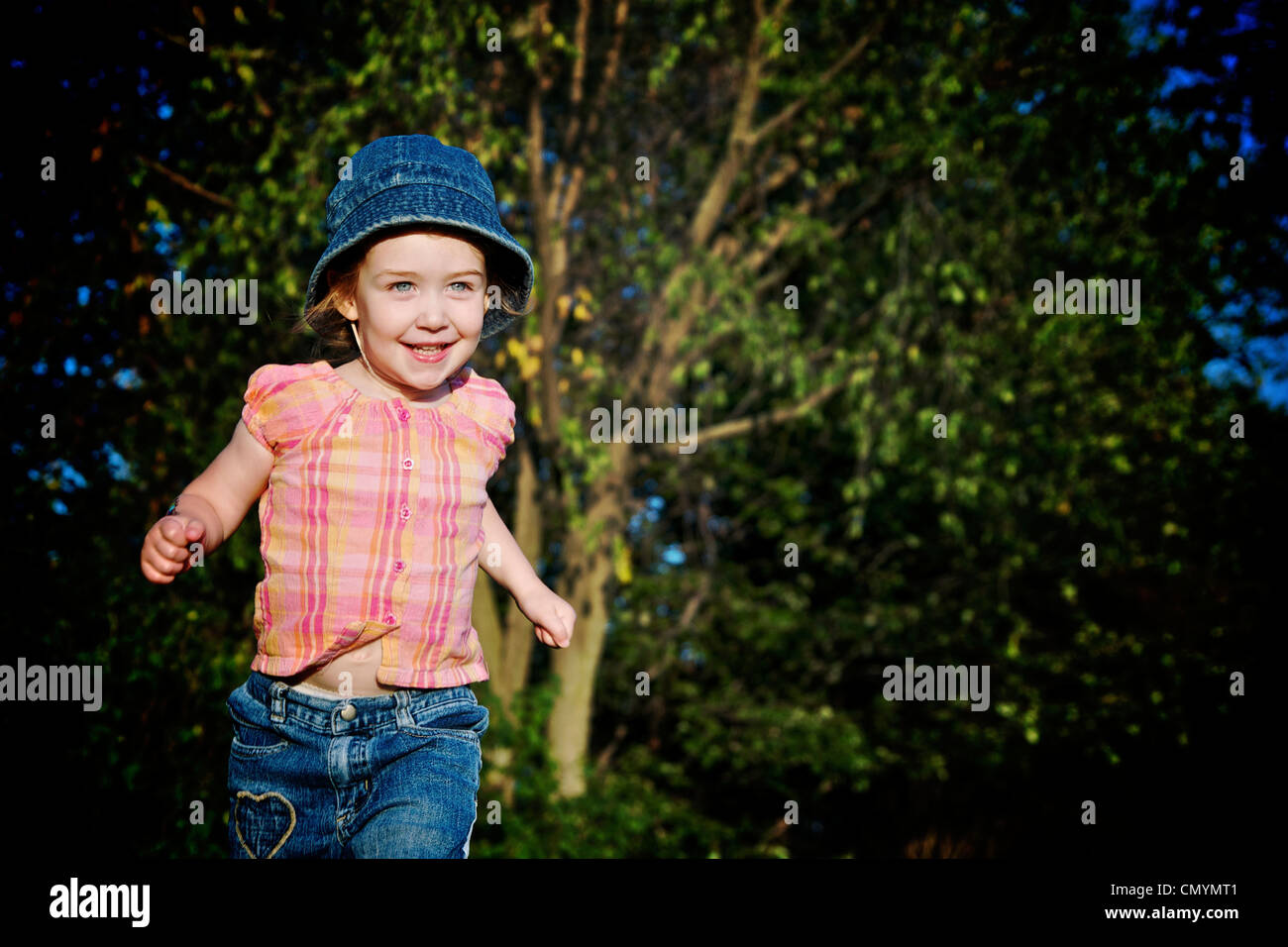 Young girl with blue denim hat running, Otterburn Park, Quebec Stock Photo