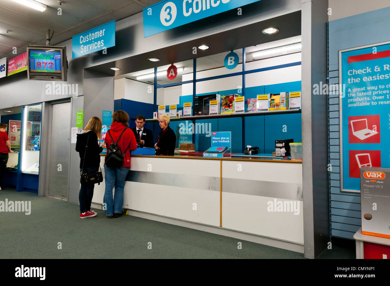 Two customers talking to Customer Services counter in Argos, UK Stock