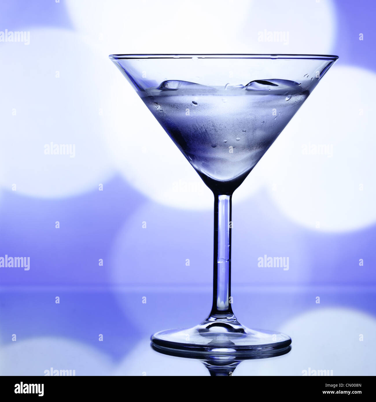 Cocktail glass with ice and holiday lights in the background Stock Photo