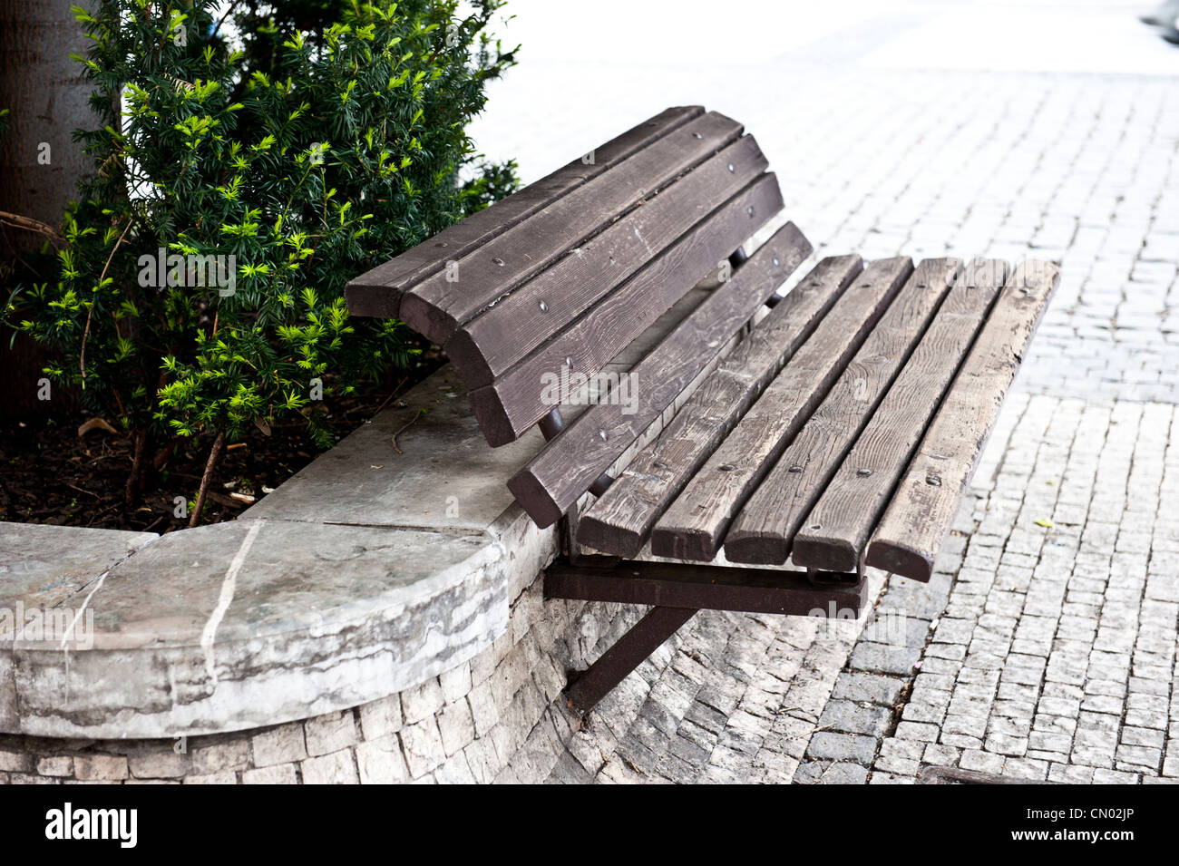 Side shot of an empty, wooden sidewalk bench - in front of a bush. Stock Photo