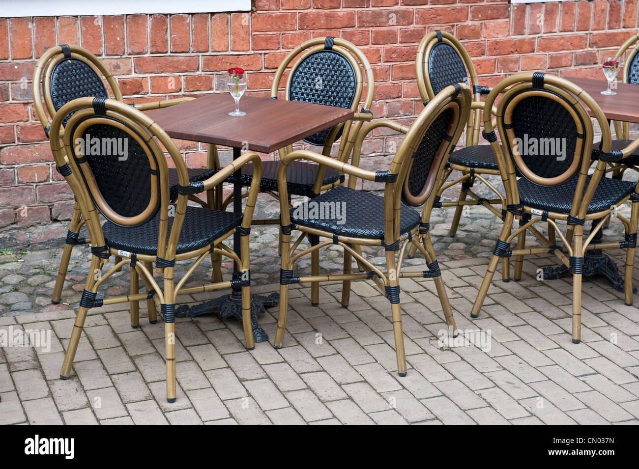 Empty square tables and chairs with rose centerpieces in wine glasses on a patio outside of a restaurant. Stock Photo