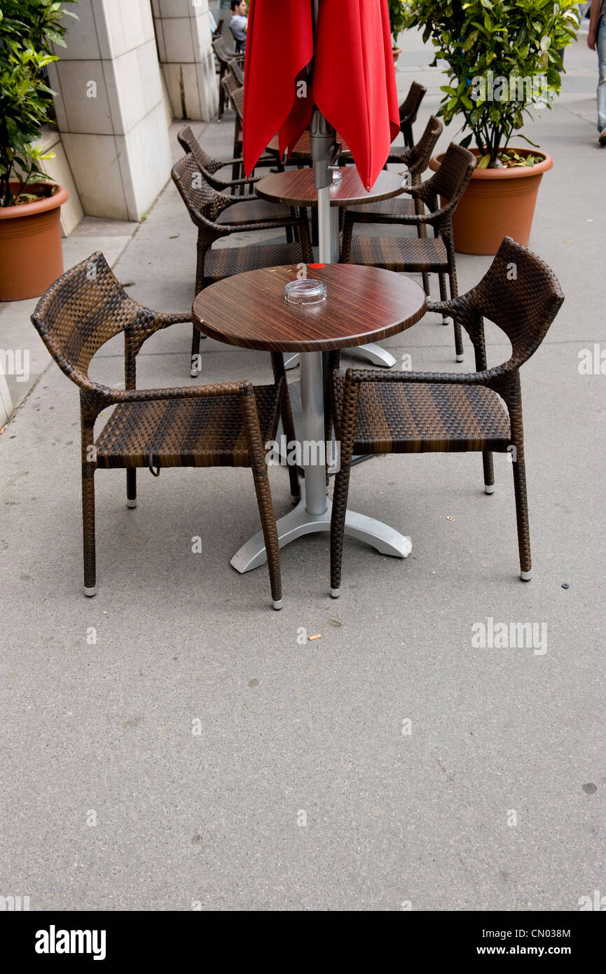 A centered color shot of a cafe table, with a red umbrella in a row with other like brown cafe tables. Stock Photo