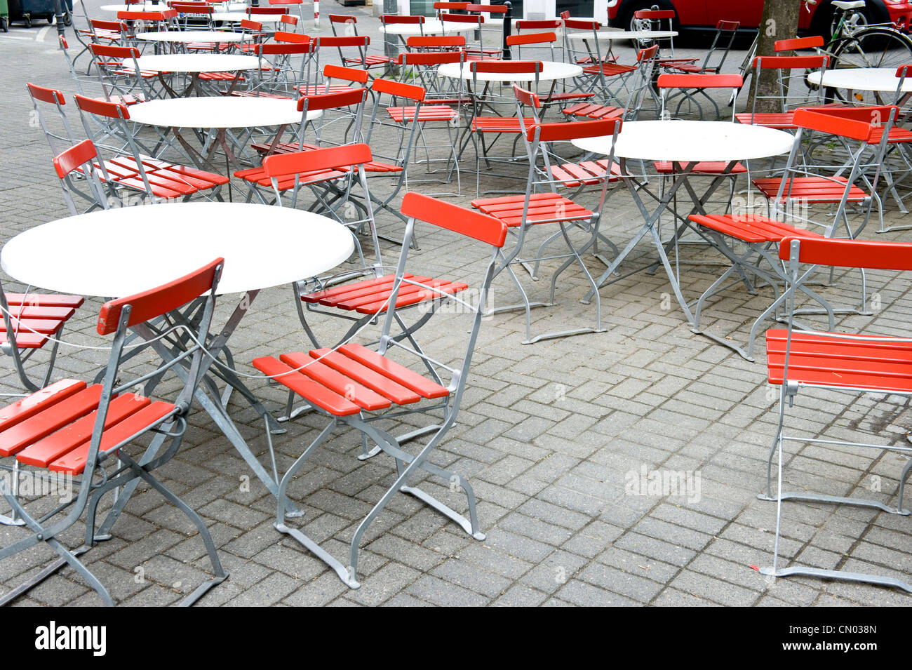 An empty cafe sidewalk sitting area with white tables and red chairs. Stock Photo