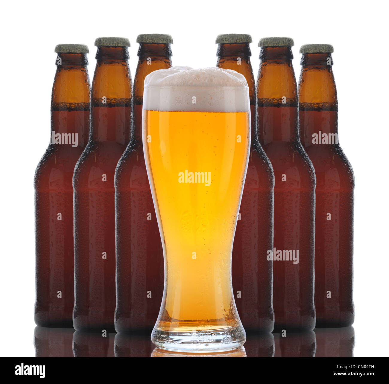 A glass of foamy beer with six brown bottles grouped behind over a white background with reflections Stock Photo