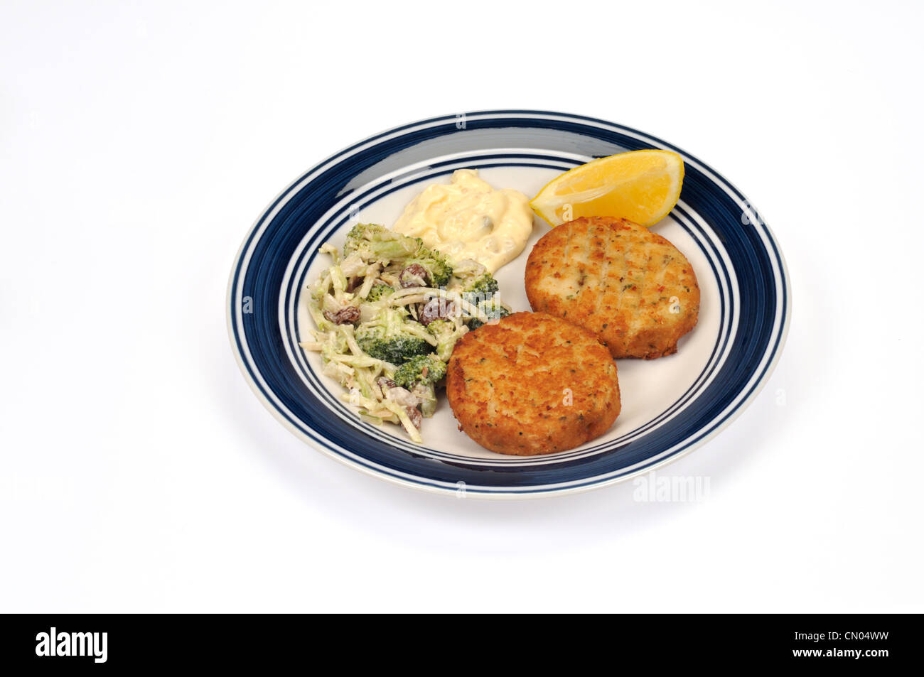 Plate of fishcakes with a broccoli crunch salad, tartar sauce and a lemon wedge Stock Photo
