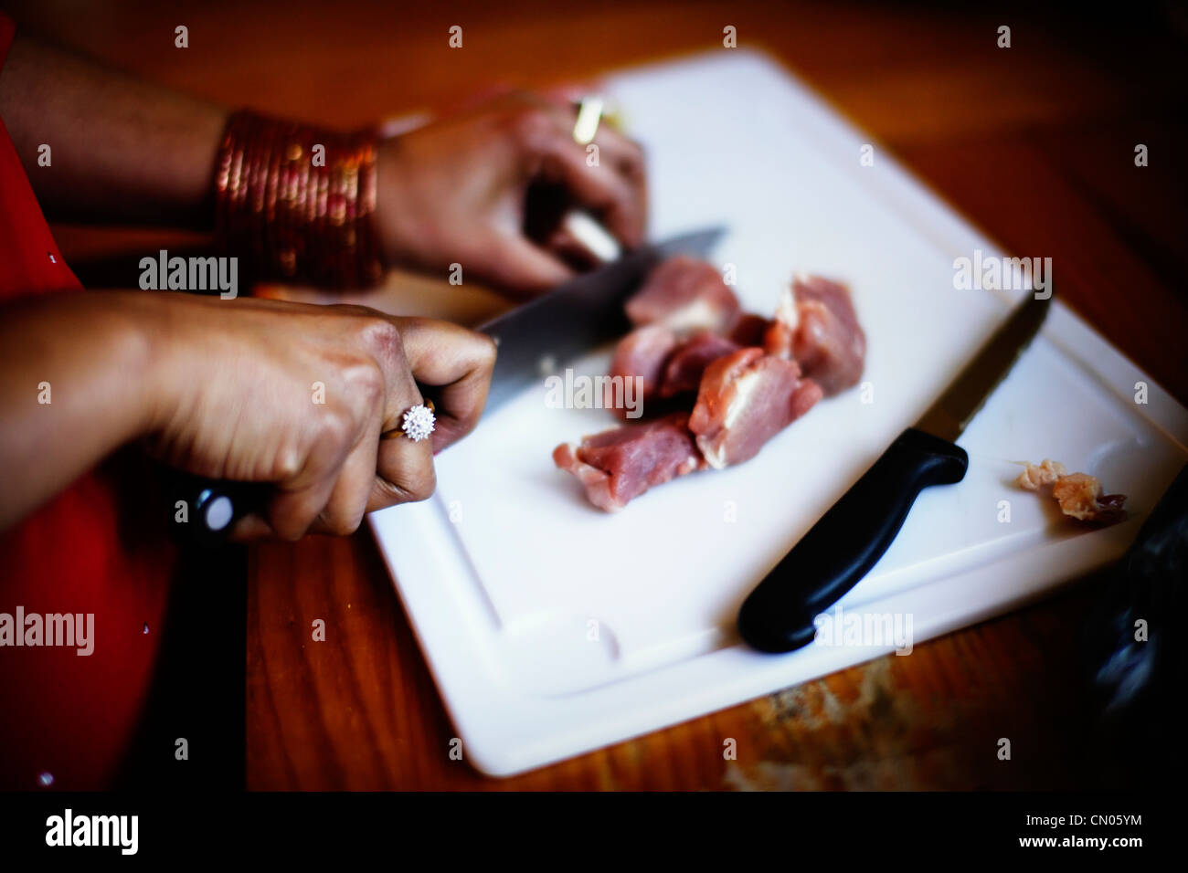 Punjabi woman wearing bangles and jewellery cuts meat with knife. Stock Photo