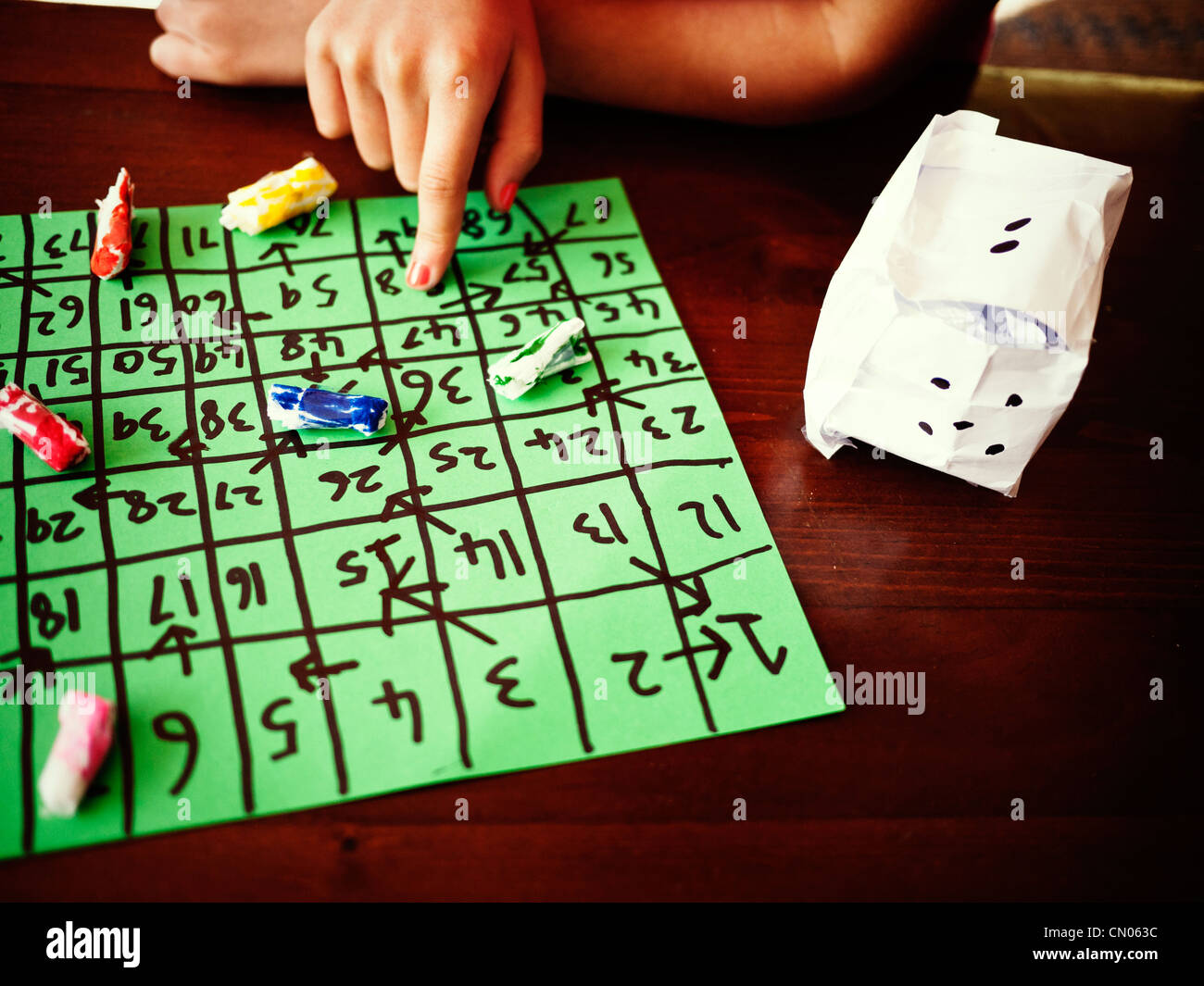 Girl plays her homemade board game with homemade counters and dice. Stock Photo