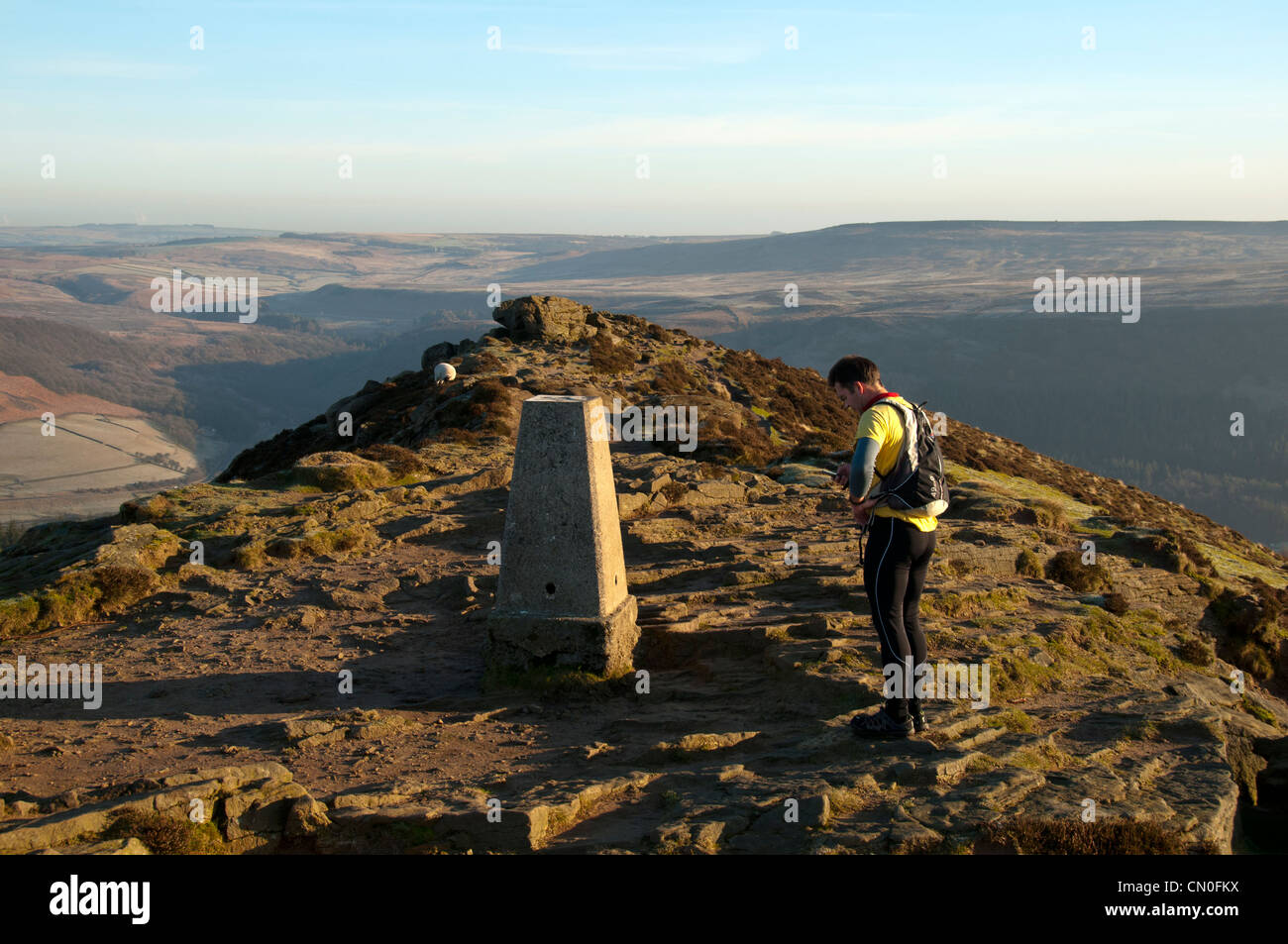 A fell runner at the trig point, summit of Win Hill, near Hope, Peak District, Derbyshire, England, UK. Hope Valley behind. Stock Photo
