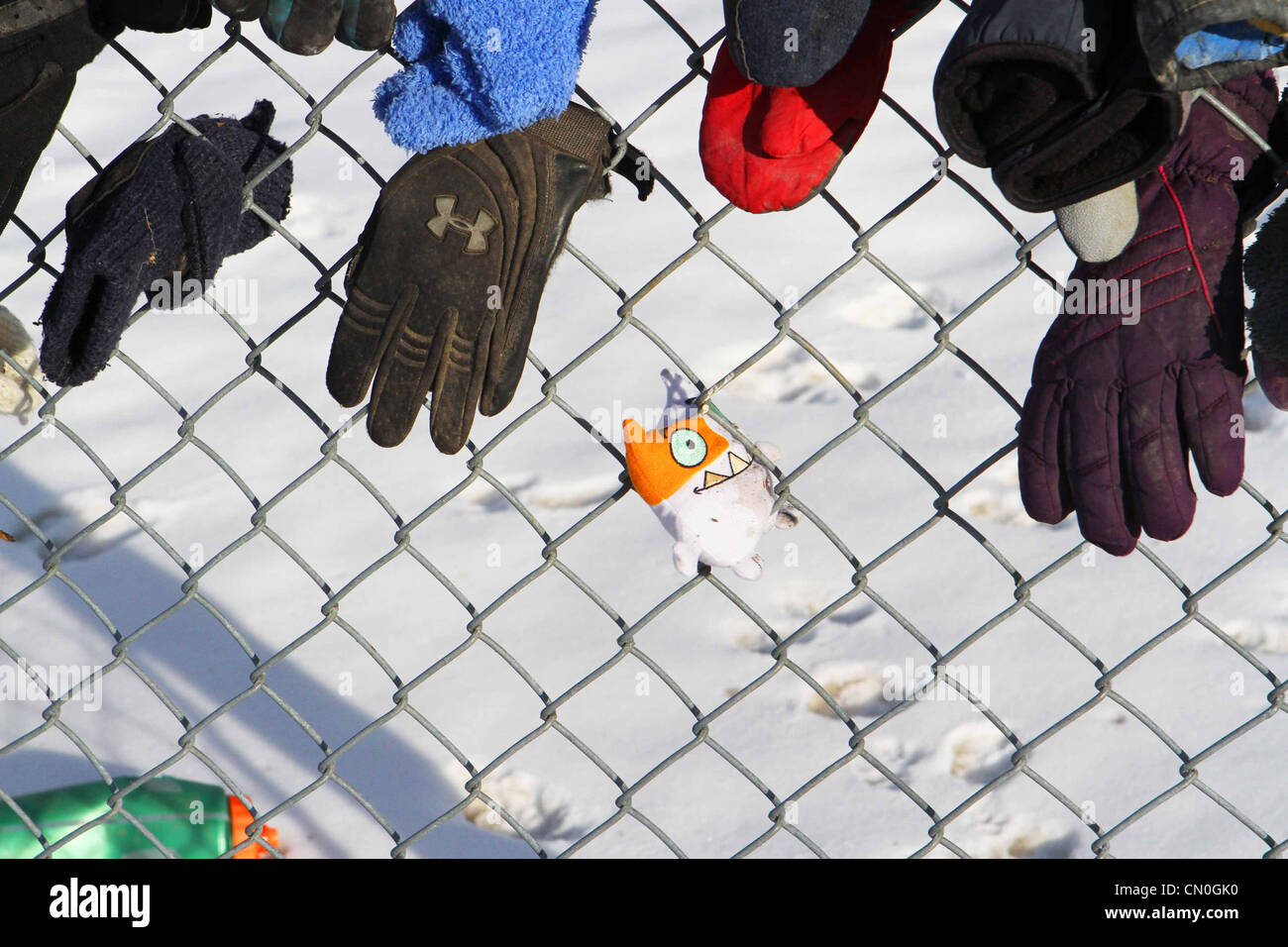Lost mittens and hats by a park pathway attached to a chain link fence Stock Photo