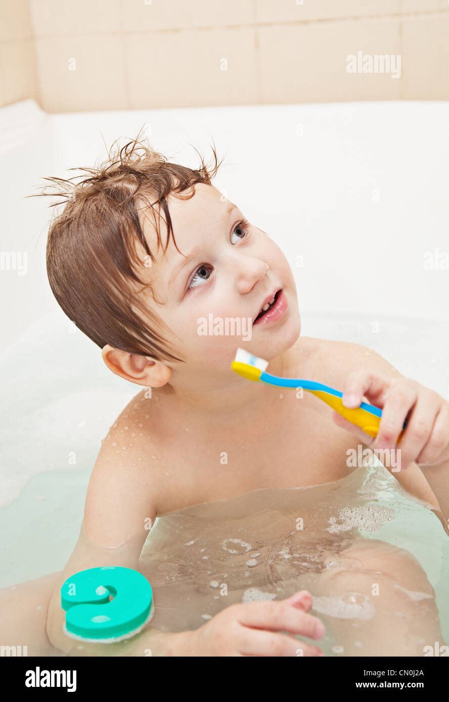 Cute little boy sitting in the full bath and holding toothbrush Stock Photo