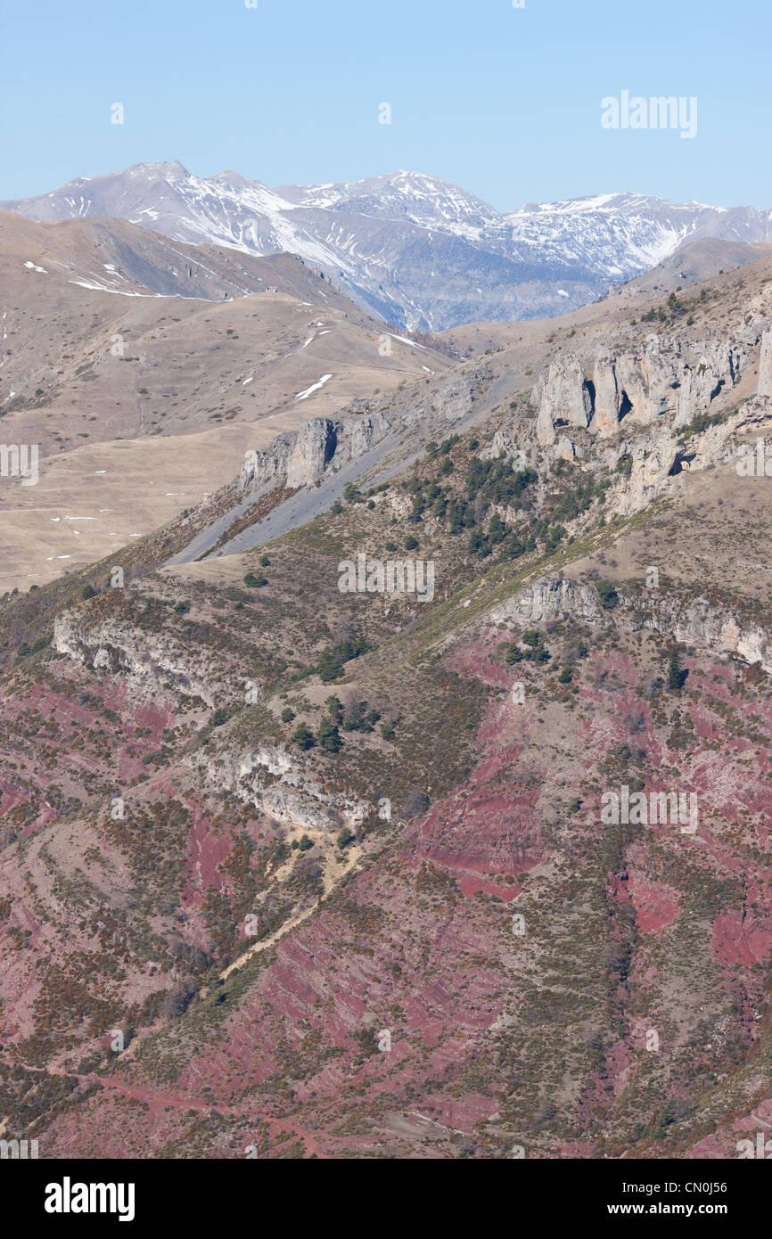 AERIAL VIEW. Red sedimentary rock (pelite) in the foreground with the snow-covered peaks of the southern Alps. Alpes-Maritimes, France. Stock Photo