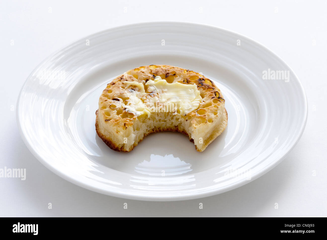 one crumpet on a plate with a bite taken Stock Photo