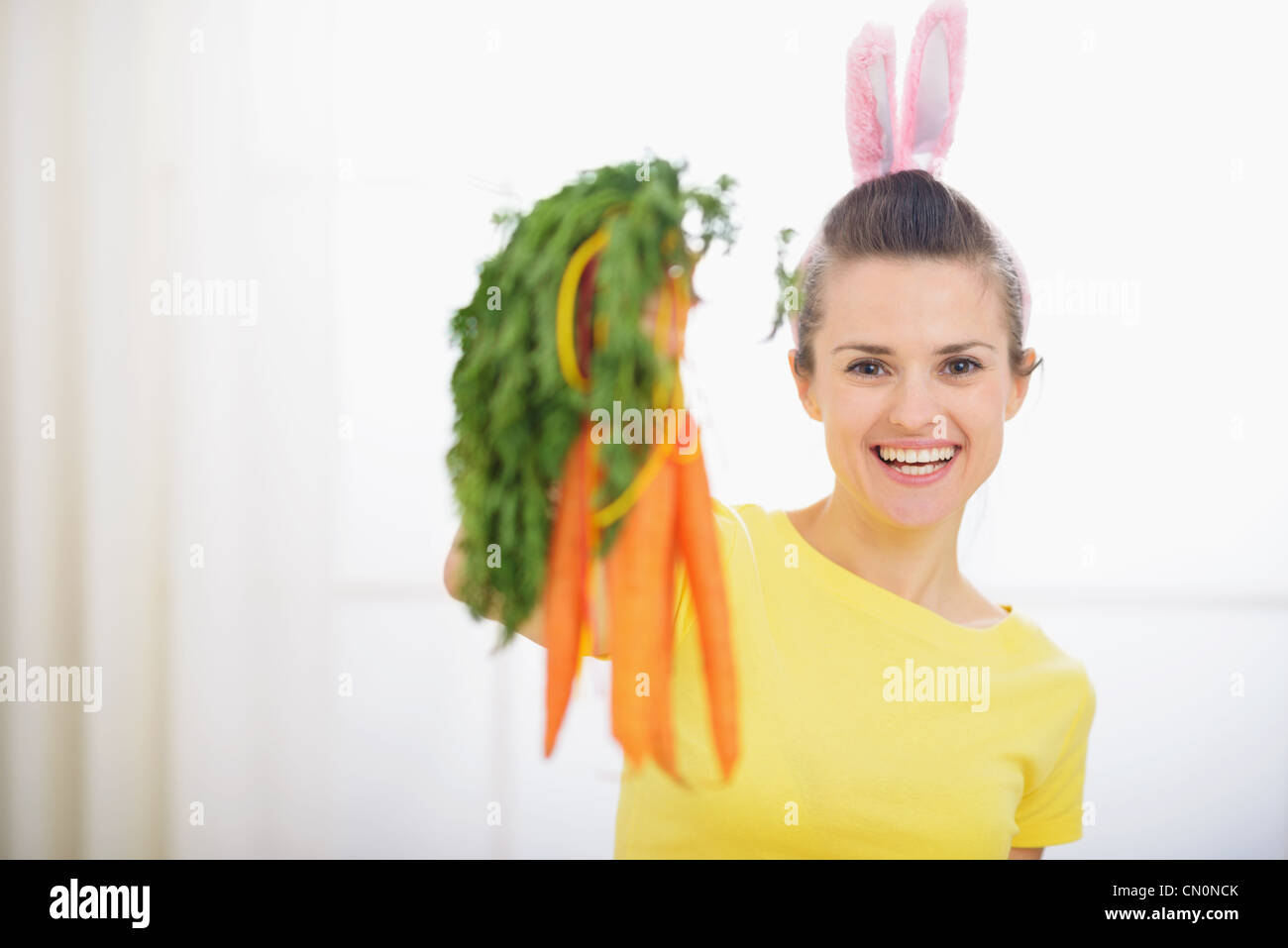 Smiling woman in rabbit ears showing bunch of carrots Stock Photo