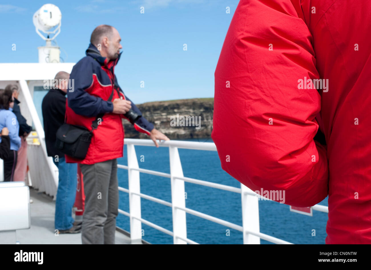 Tourists watch the land pass by as they sail on a passenger ferry towards the Orkney Islands in Scotland Stock Photo