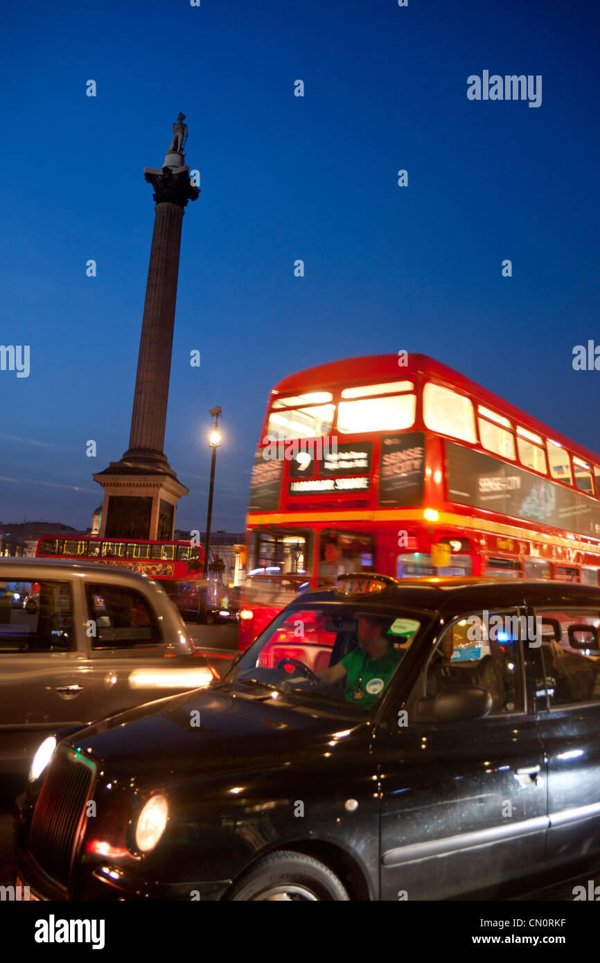 Nelson's Column and Trafalgar Square at night with red London bus and black taxi cab passing London England UK Stock Photo