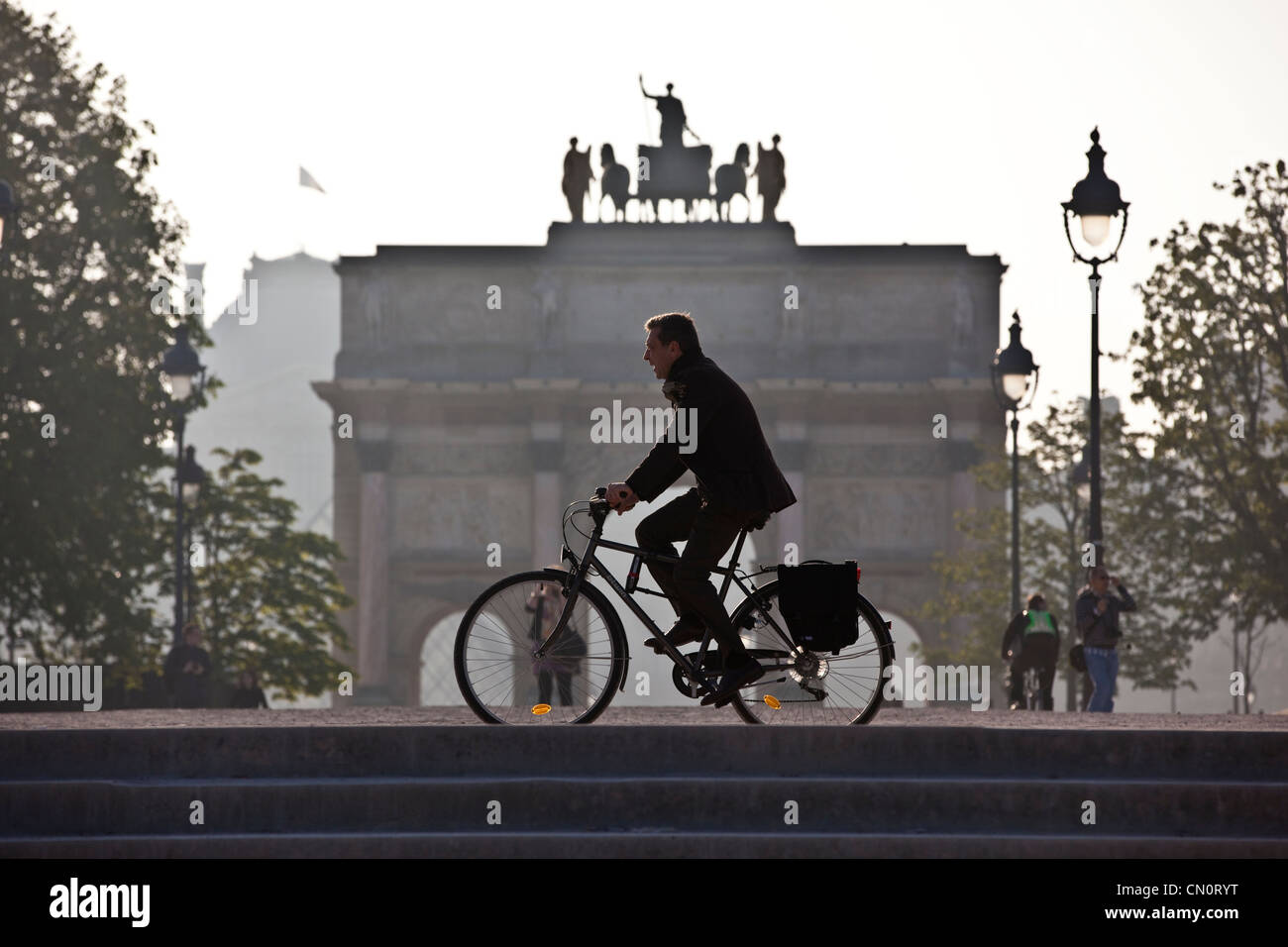 An early morning commuter cycles past the Arc de Triomphe du Carrousel in Jardin desTuileries, Paris, France. Stock Photo