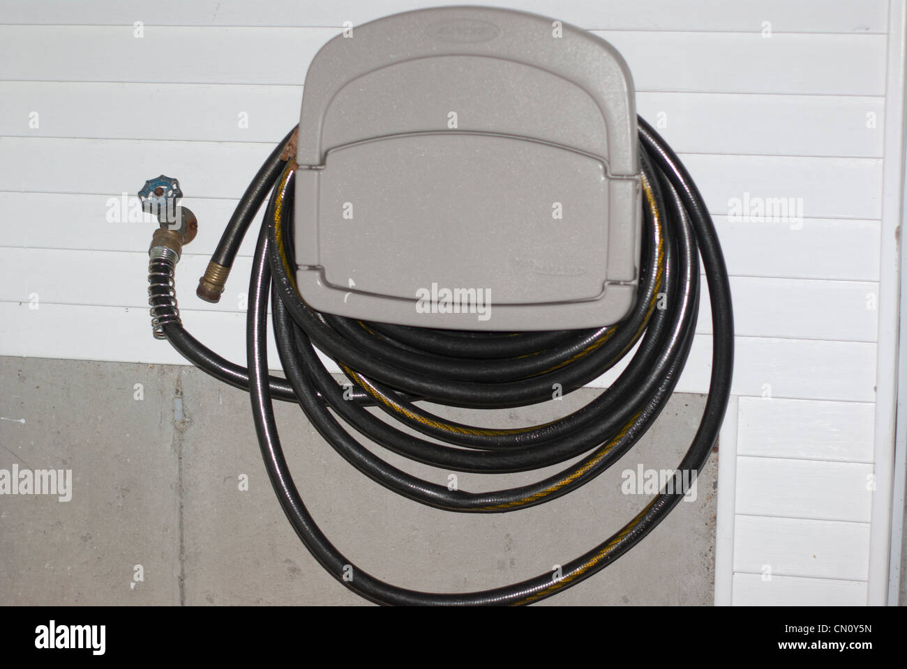Hose hanging on exterior wall of white vinylsided house Stock Photo