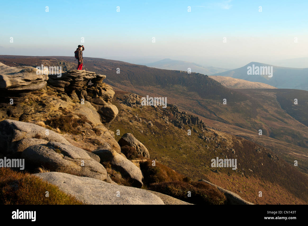 A walker stands on the edge of the Kinder Scout plateau above Edale, Peak District, Derbyshire, England, UK. Stock Photo