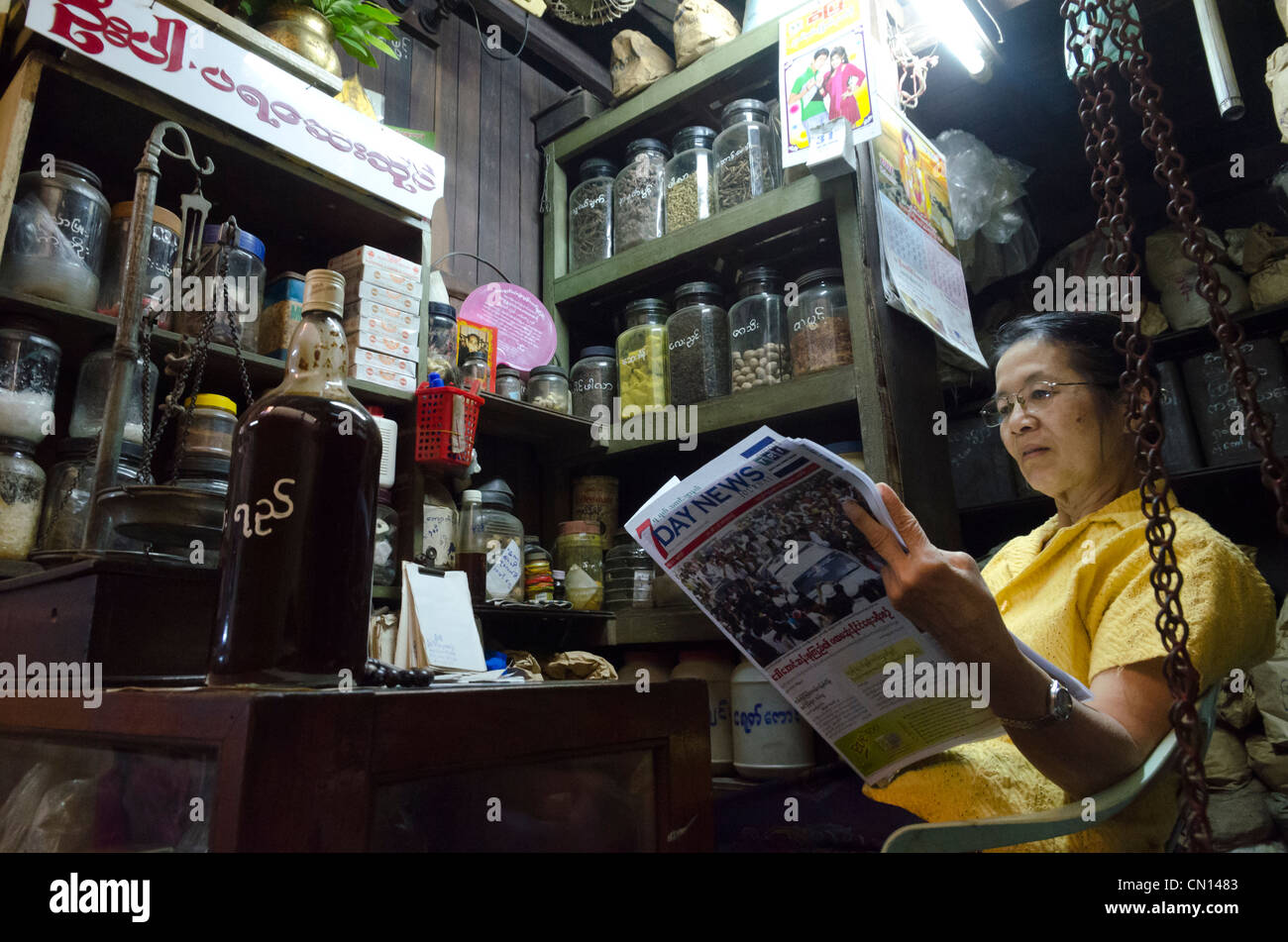 Woman reading the newspaper in her market stall. Theingyi zei market. Yangon. Myanmar. Stock Photo