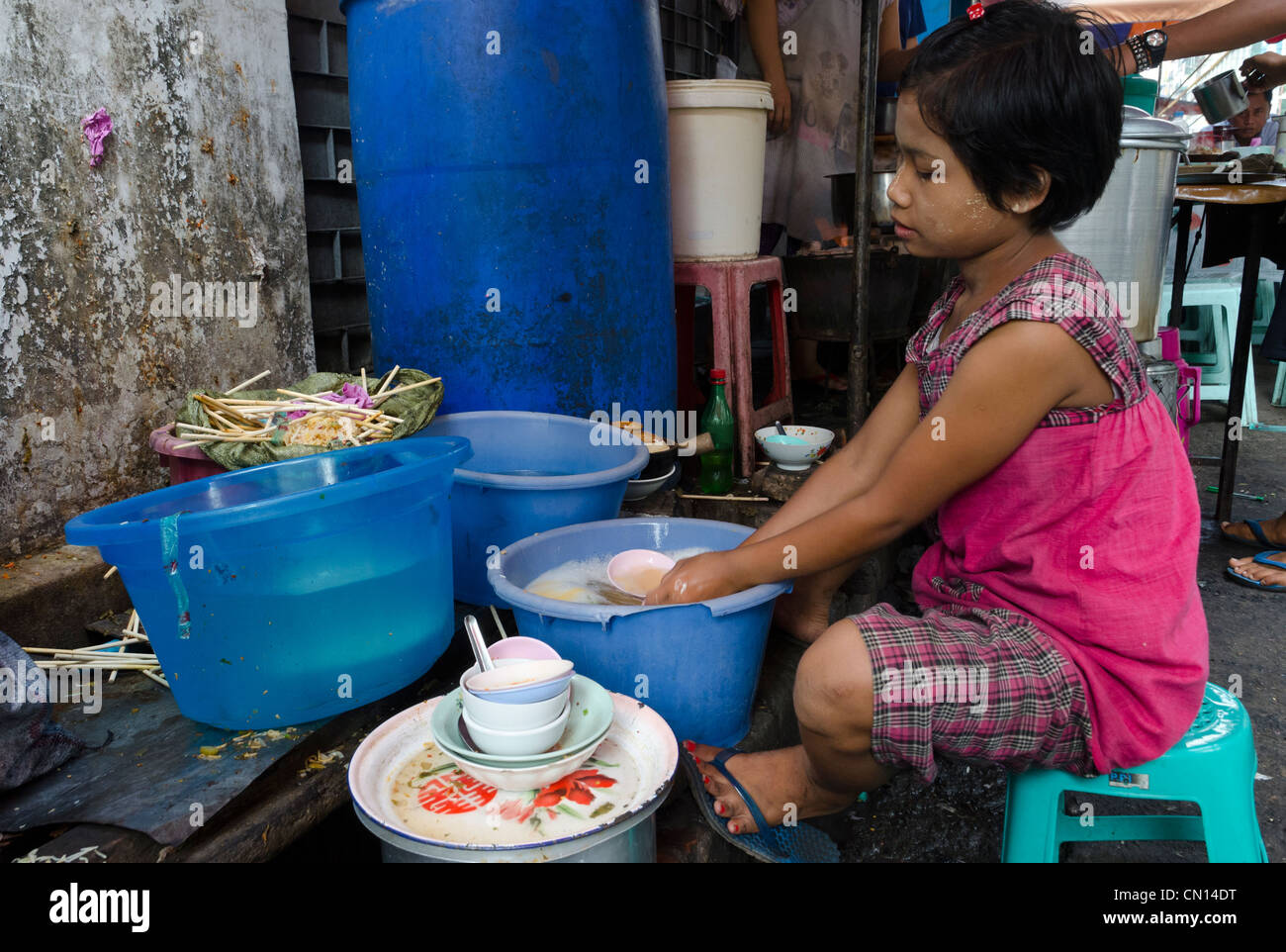 Female child washing up the dishes at a food stall in the streets of Yangon. Myanmar. Stock Photo