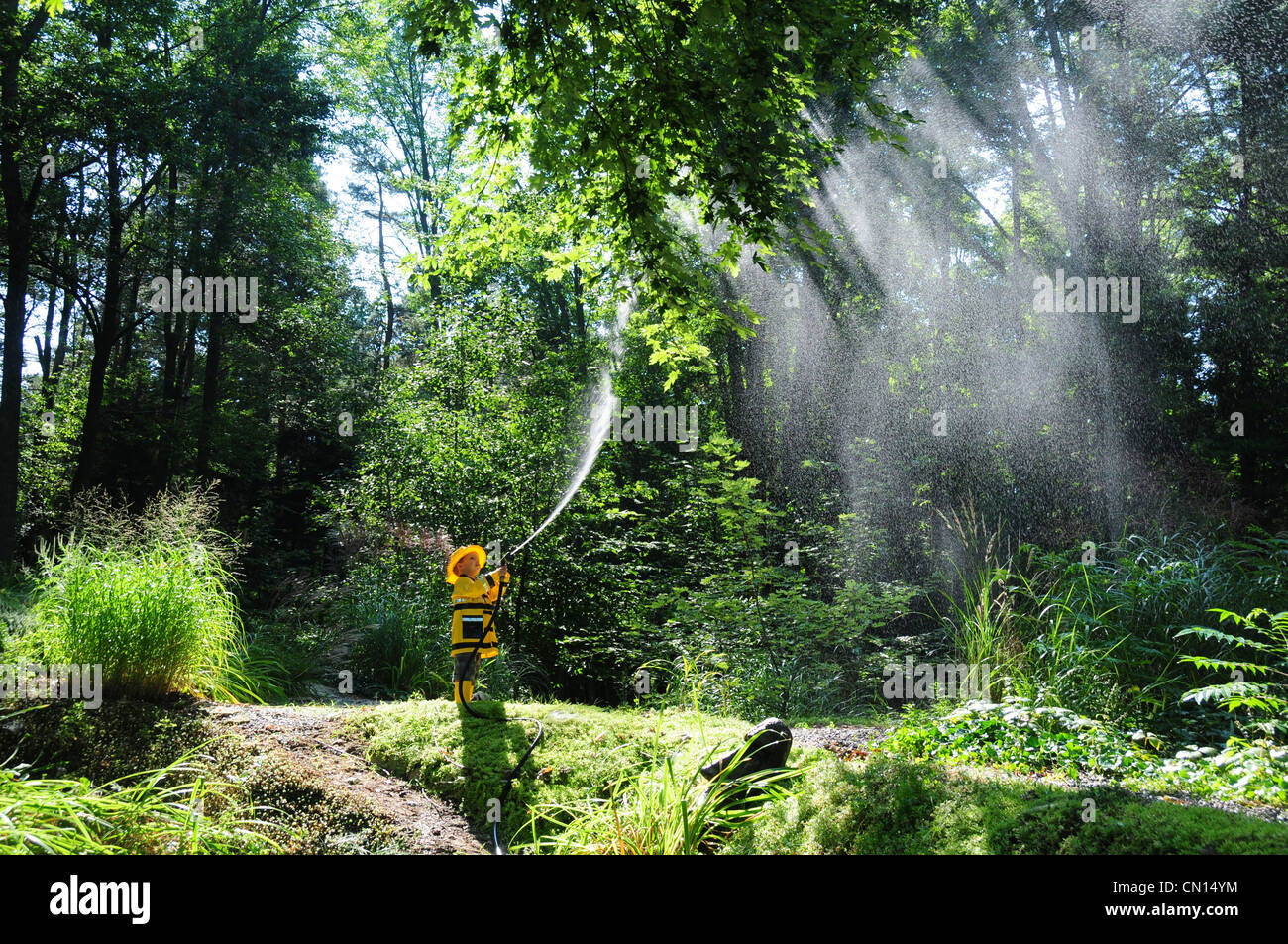 Little boy dressed as a fireman spraying water into trees, Simcoe, Ontario Stock Photo