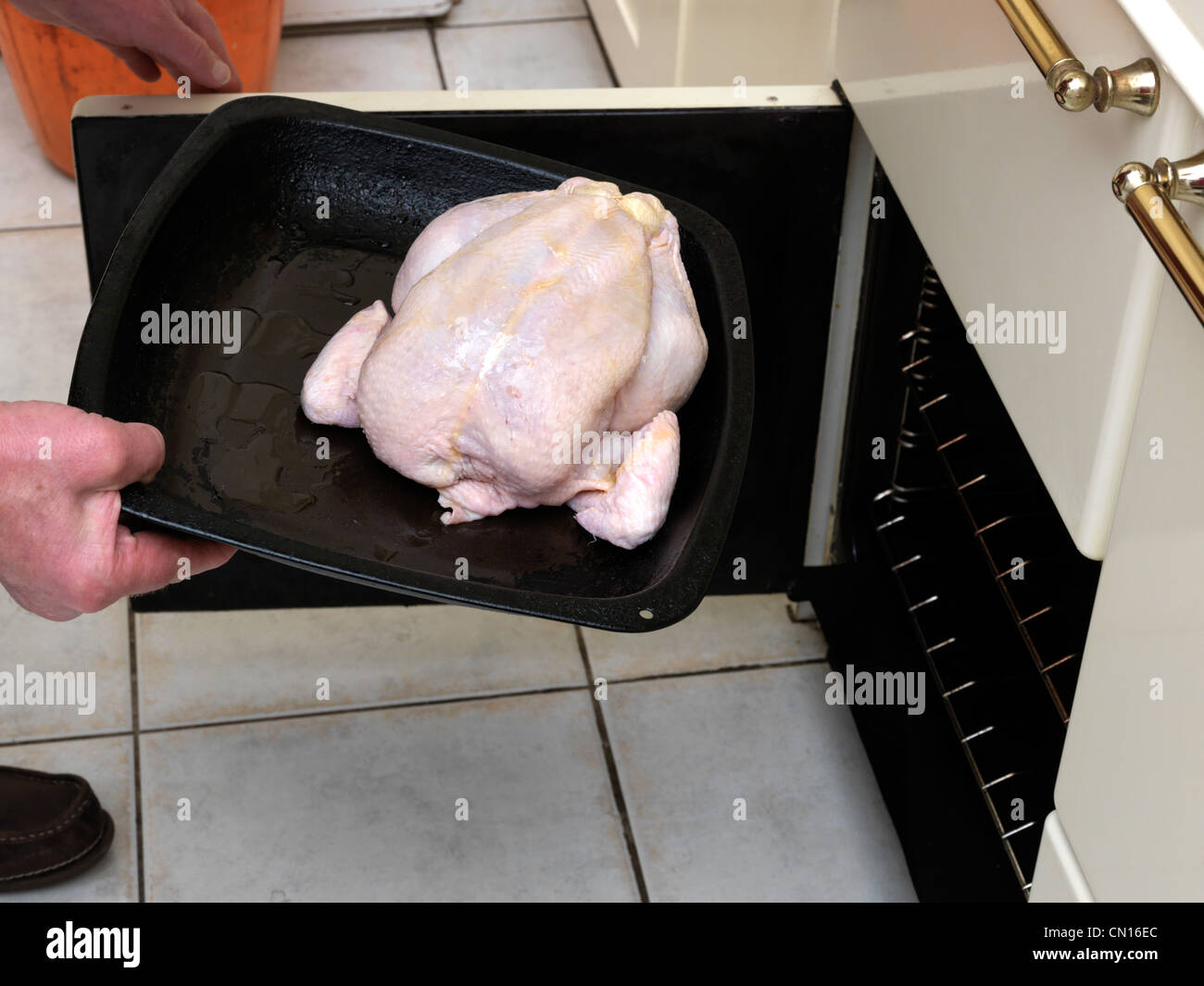 Raw chicken in roasting tin being placed into an oven hires stock