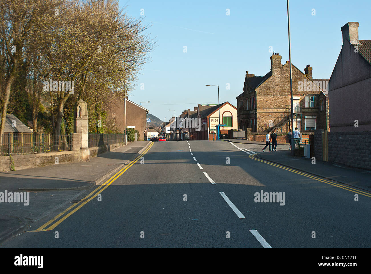 Urban street scene from middle of the road showing houses cars and shops and people walking in the distance Stock Photo