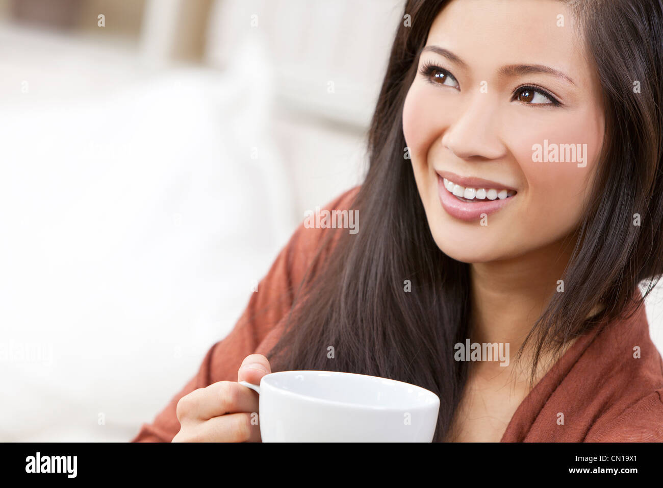 A beautiful young Chinese Asian Oriental woman with a wonderful toothy smile drinking tea or coffee from a white cup and saucer Stock Photo