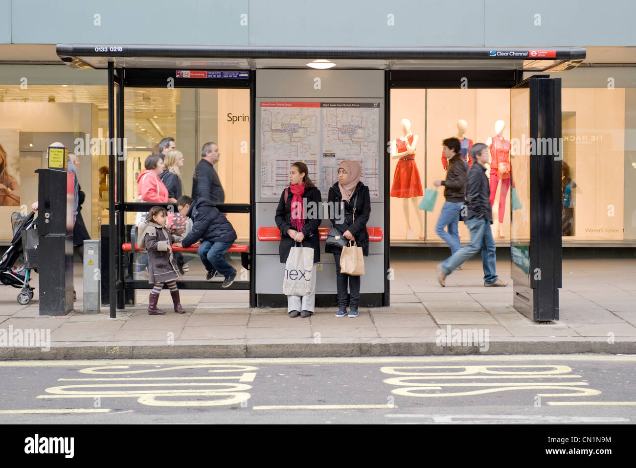 Oxford Street London West End two young ethnic girls ladies women females with children wait in bus stop shelter for bus Stock Photo