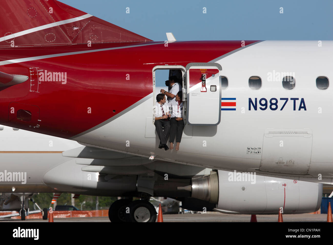 Aircrew take a break sitting at the rear door of a passenger jet airliner at Jamaica's Kingston Airport Stock Photo