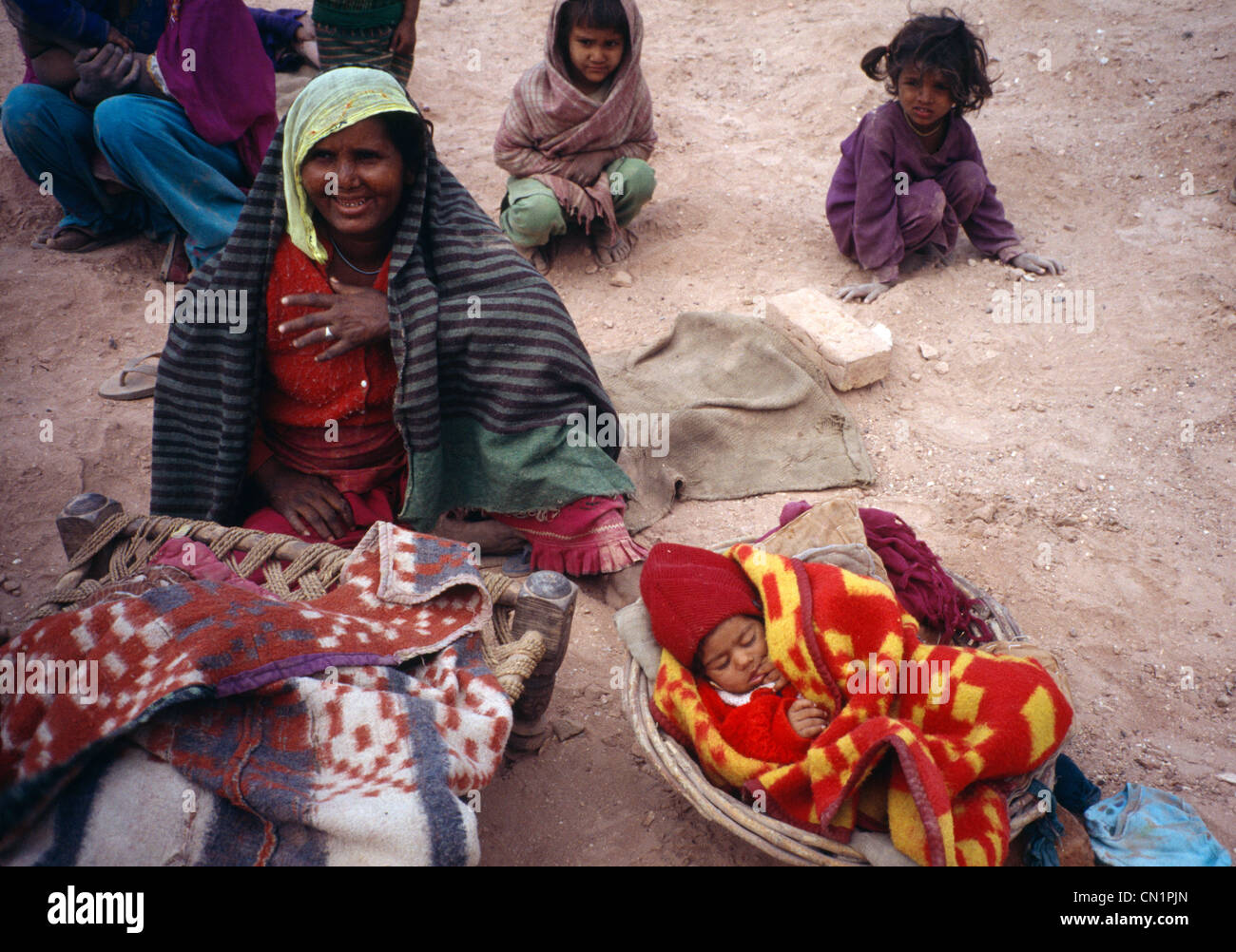 Amritsar punjab India Brickworks Family Sitting On Ground Baby Wrapped Up In Basket And Children Behind Stock Photo