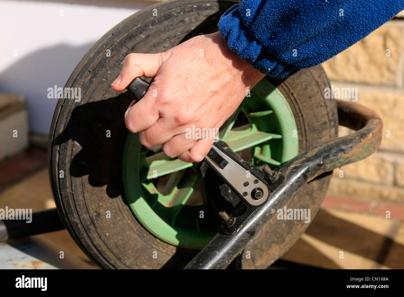 A man uses an socket wrench to remove the wheel from a garden barrow