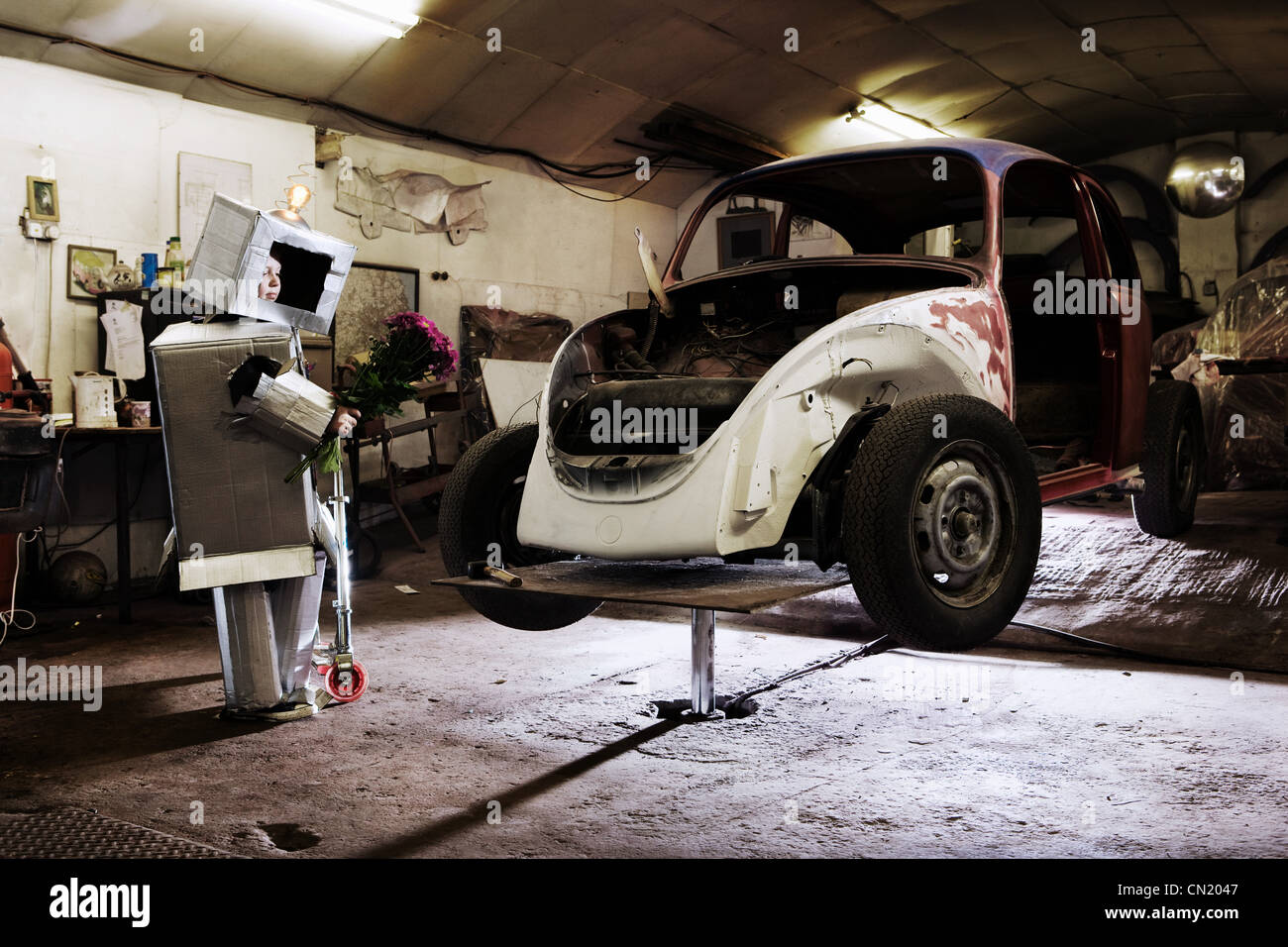 Boy dressed as robot holding bunch of flowers with old car in garage Stock Photo