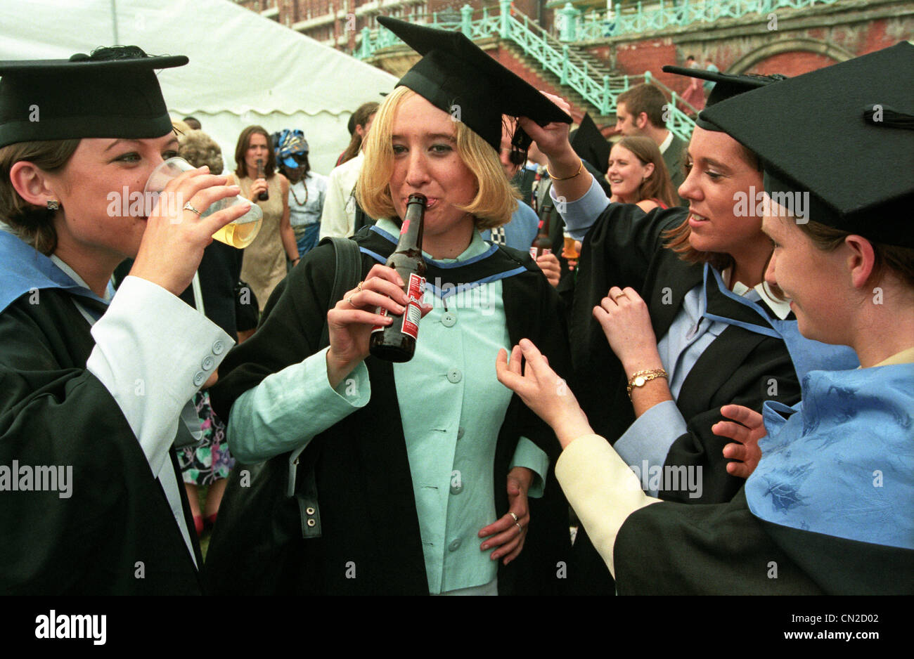 A female graduate with her gown and mortar board celebrates her degree with a bottle of beer at the University of Brighton. Stock Photo