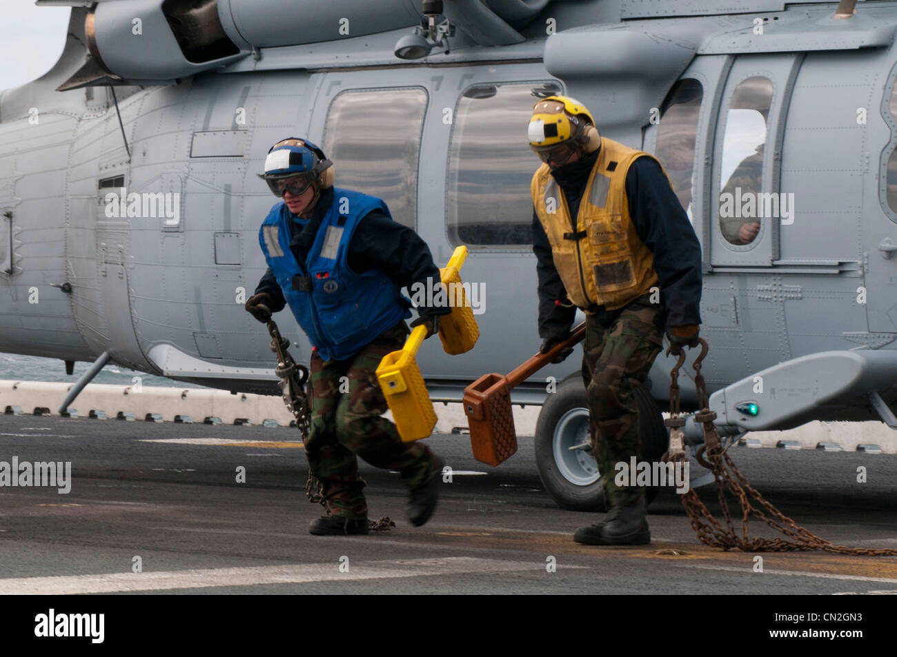 Aviation boatswain's mates run away from an MH-60S Knight Hawk helicopter after removing chocks and chains making the aircraft ready for take-off on the flight deck of the amphibious assault ship USS Kearsarge (LHD 3). Kearsarge is underway conducting Afloat Training Group 1.4 basic phase training. Stock Photo