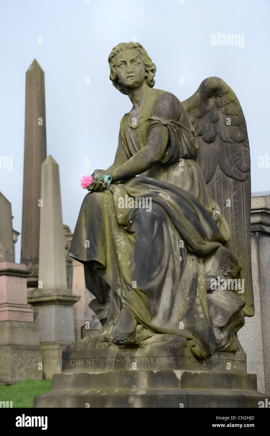 The statue of an angel, with an artificial flower in her hand, resting on an monument in the Glasgow Necropolis. Stock Photo